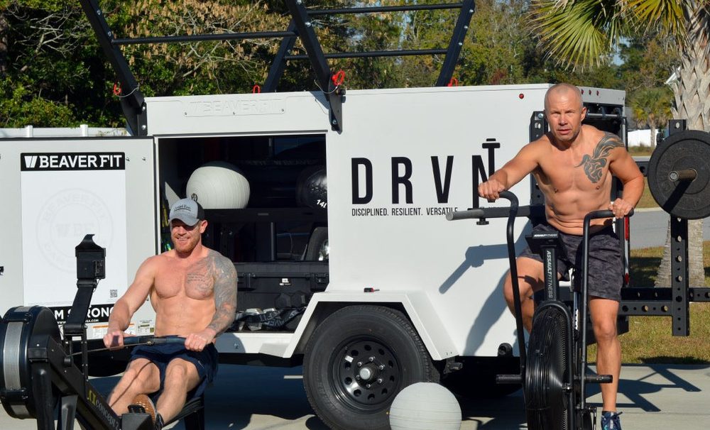 Two athletes training on a rower and air bike at the DRVN trailer