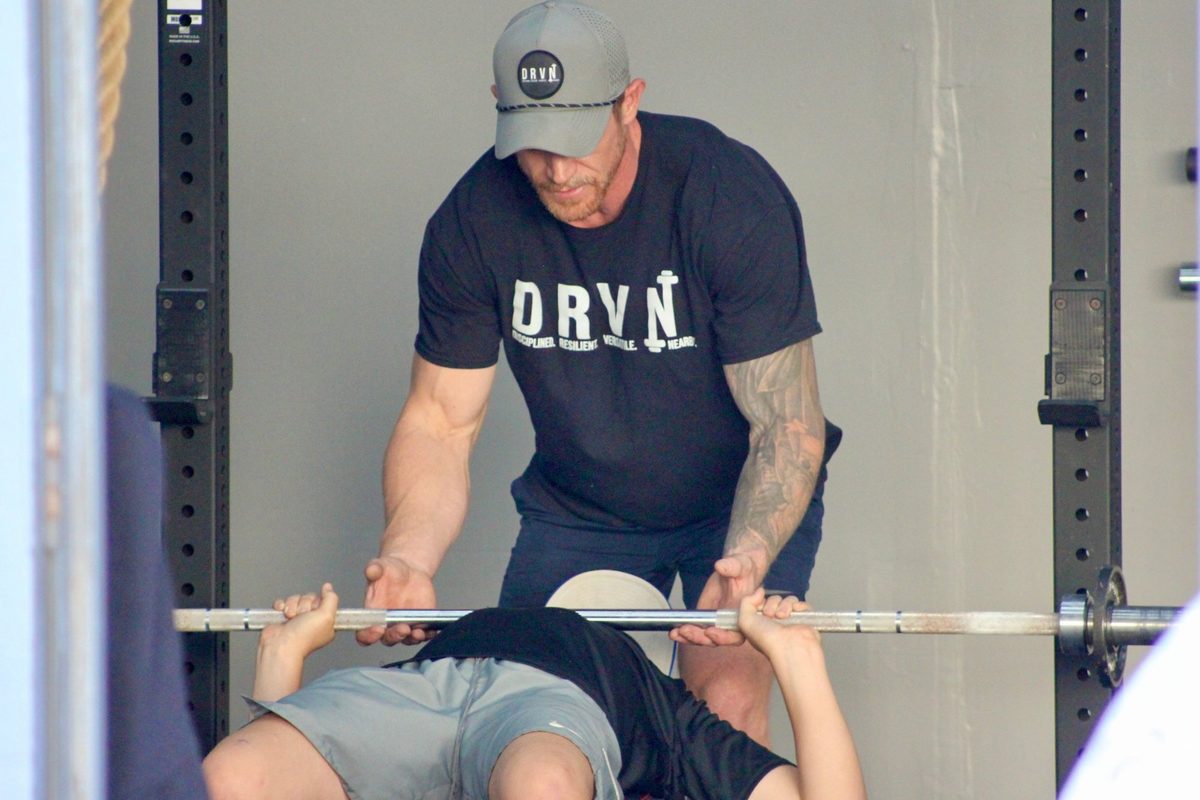Coach spotting a youth athlete bench pressing at DRVN