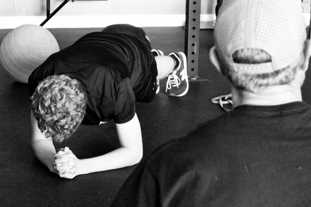 Youth athlete holding a plank while a coach watches